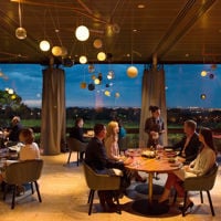 A table of four is being served at Magill Estate Restaurant with views of vines and the city's skyline.