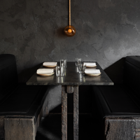 Food like charred cauliflower and fish surrounds a hand holding a crisp white wine at Arkhe.